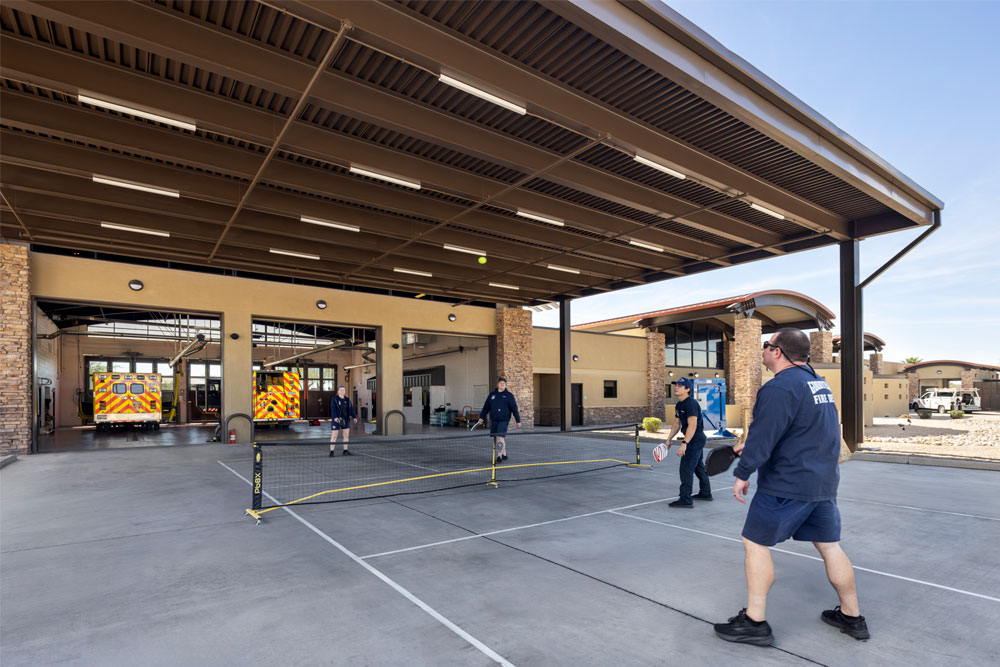 Firefighters playing pickleball under canopy behind fire station